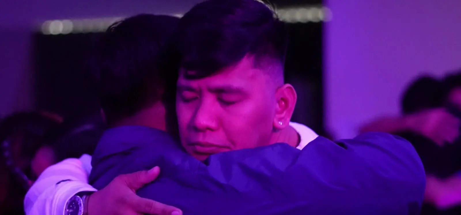 A Discovery participant in tears, held by another graduate during a breakthrough moment, lit in deep purple.